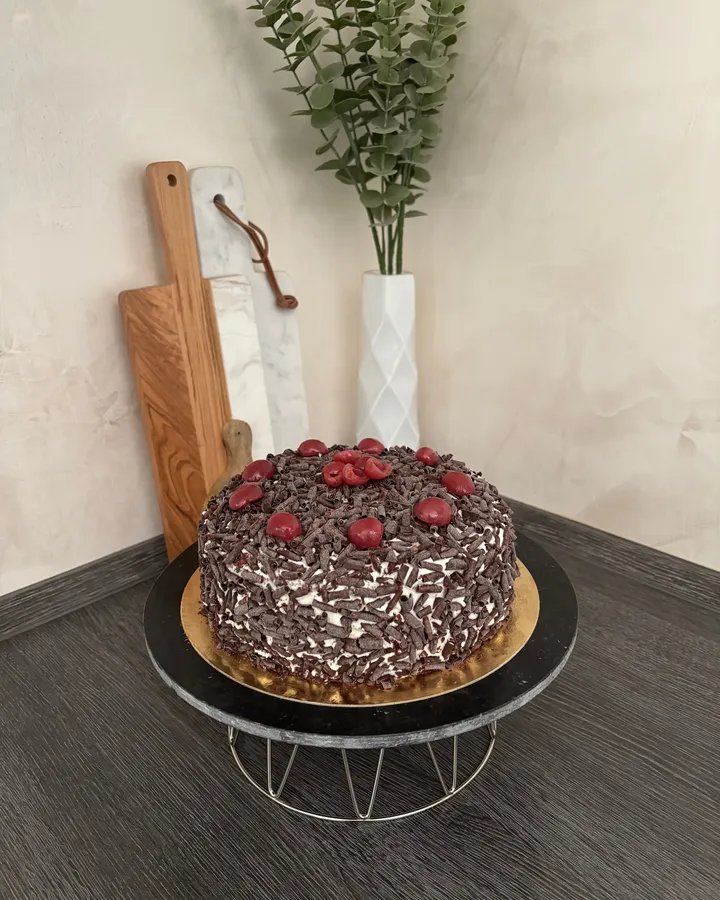 Forêt-noire entièrement masquée de copeaux de chocolat et couronnée de cerises, sur un présentoir sombre.